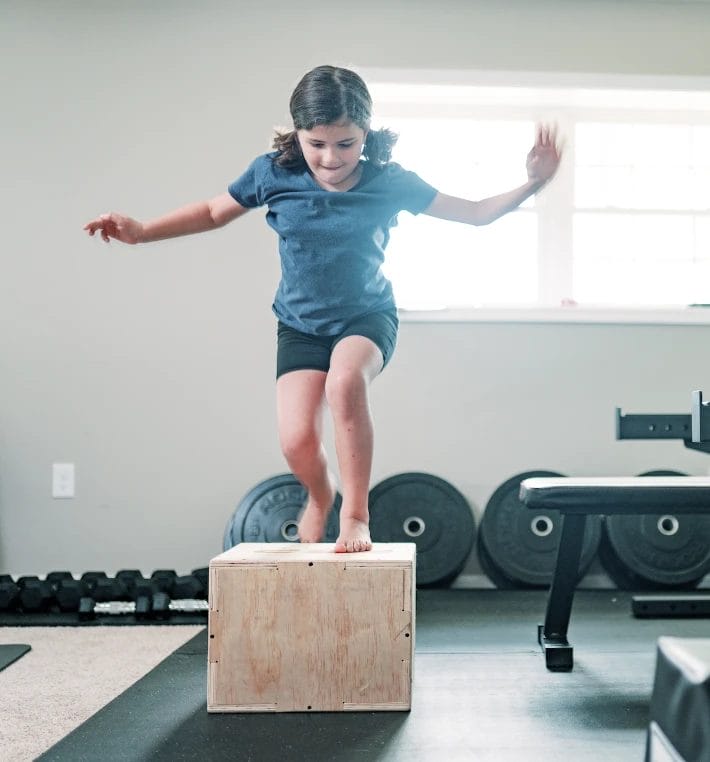 young girl performing a box jump exercise in the gym